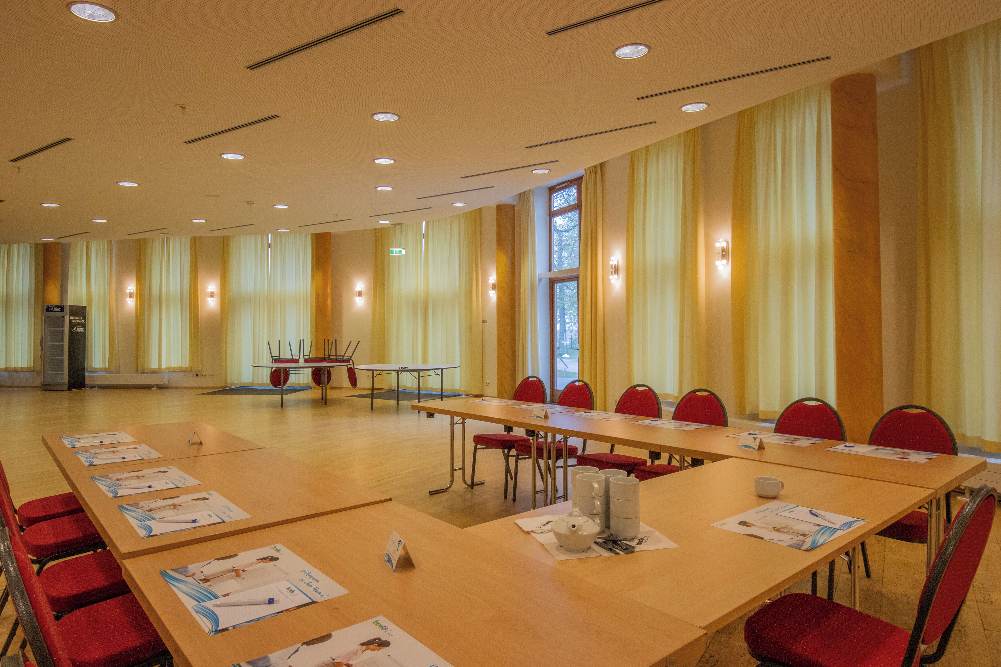 Ein Konferenzraum mit langen Tischen, roten Stühlen und Informationsbroschüren.
