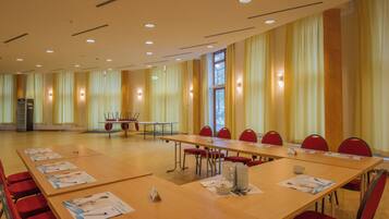 Ein Konferenzraum mit langen Tischen, roten Stühlen und Informationsbroschüren.