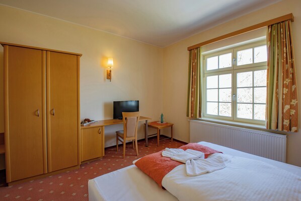 A hotel room with a bed, a desk with a chair, a television, and a window with curtains. - Seehotel Grossraeschen (Großräschen)