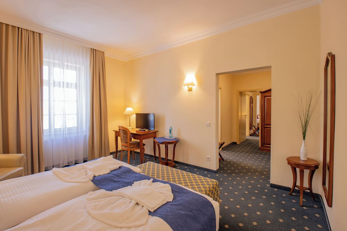A hotel room with two beds, a desk with a chair, a television, and a lamp.