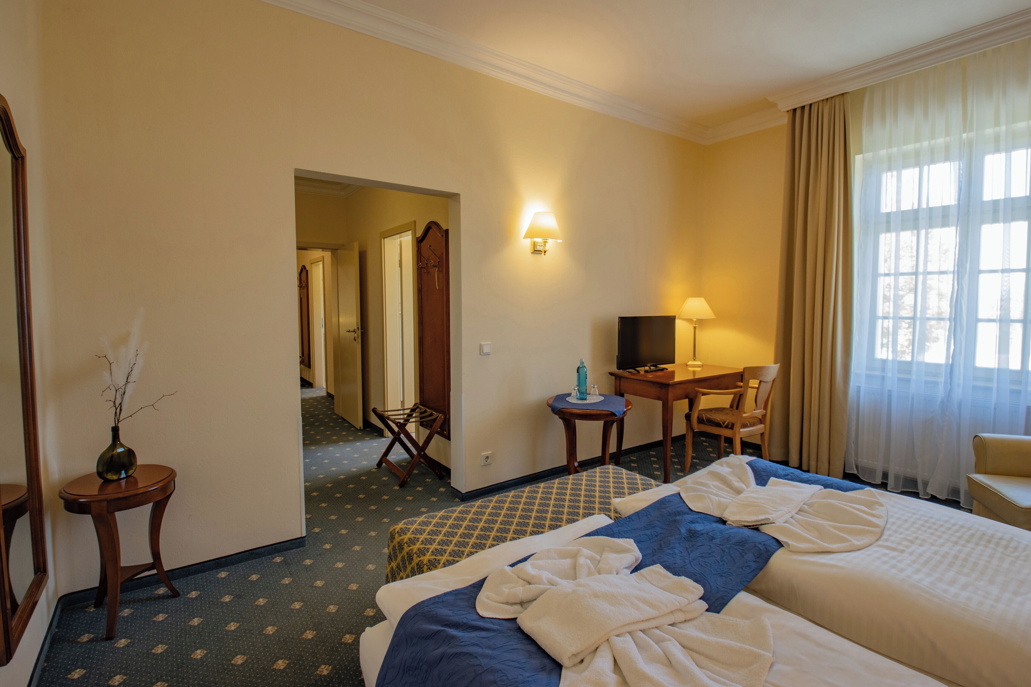 Ein Hotelzimmer mit Bett, Schreibtisch, Stuhl, Lampe und Fernseher.