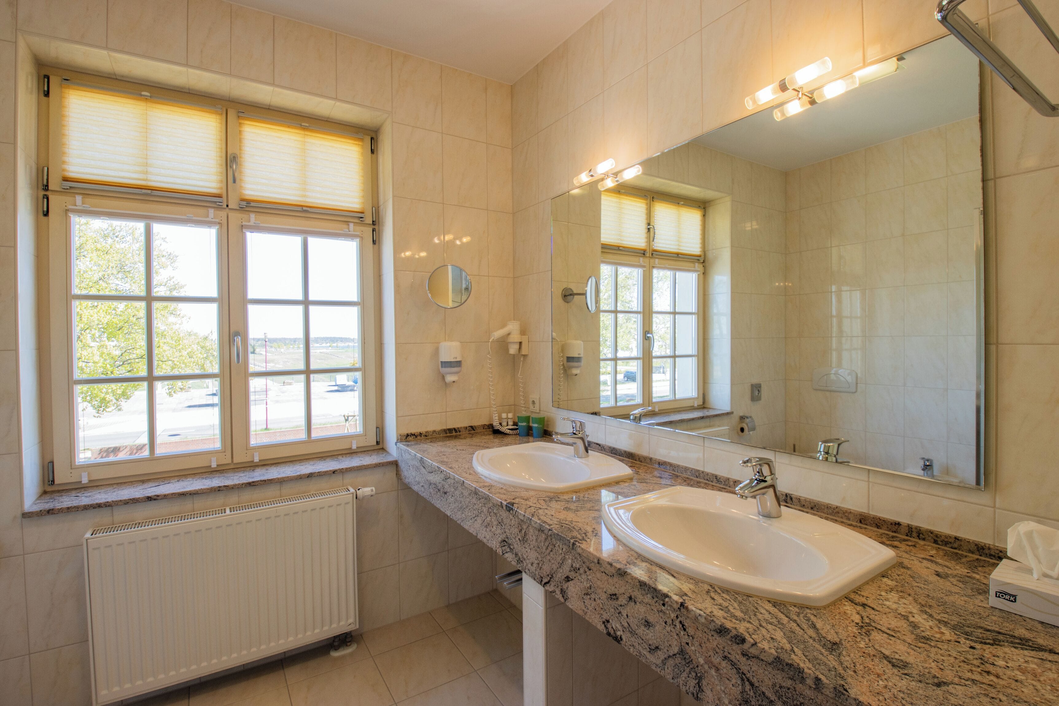 Un baño con dos lavamanos, un espejo grande y ventanas con persianas.
