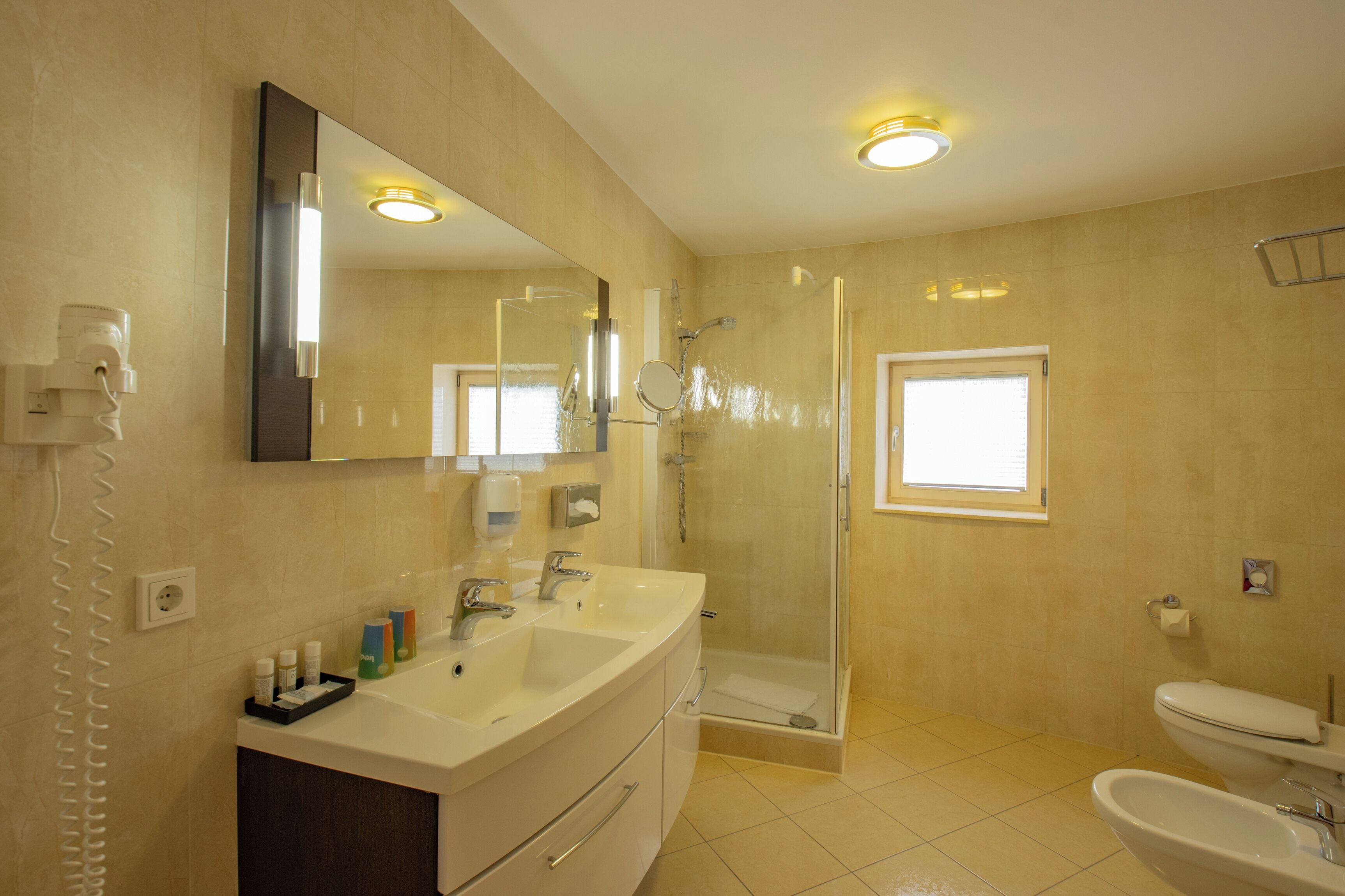 Un baño con un espejo grande, dos lavamanos, una ducha y un inodoro.