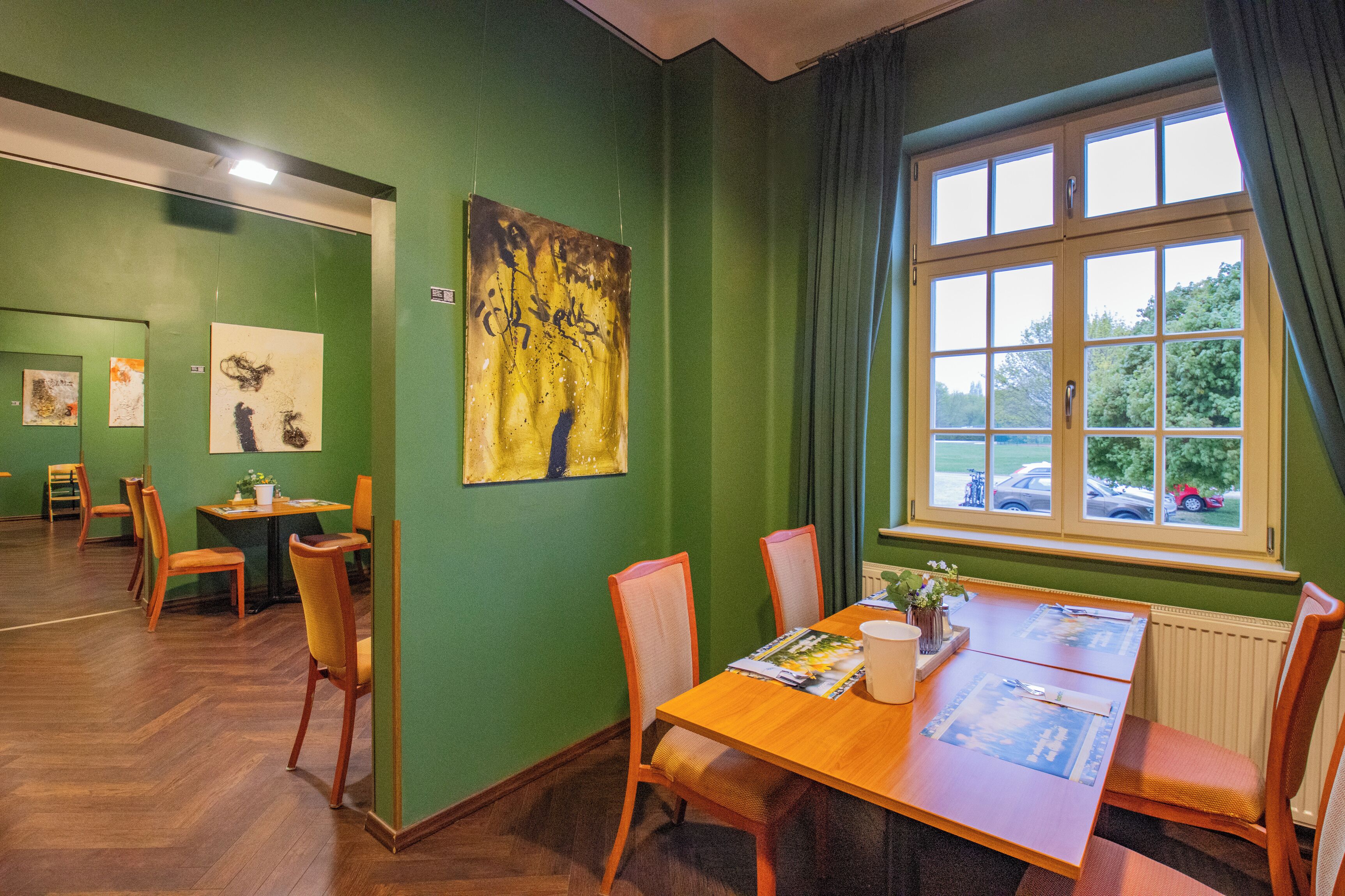 A dining area with a wooden table and chairs, a window with curtains, and artwork on the walls.
