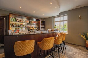 Uma área de bar com balcão, diversas prateleiras de garrafas e três banquetas.
