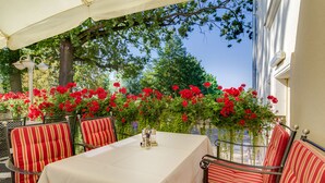 An outdoor dining area with a table and striped chairs, surrounded by red flowers and greenery. - Seehotel Grossraeschen (Großräschen)