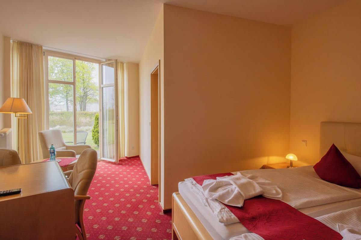 A hotel room with a bed, a desk, a chair, a window with curtains, and a red carpet.