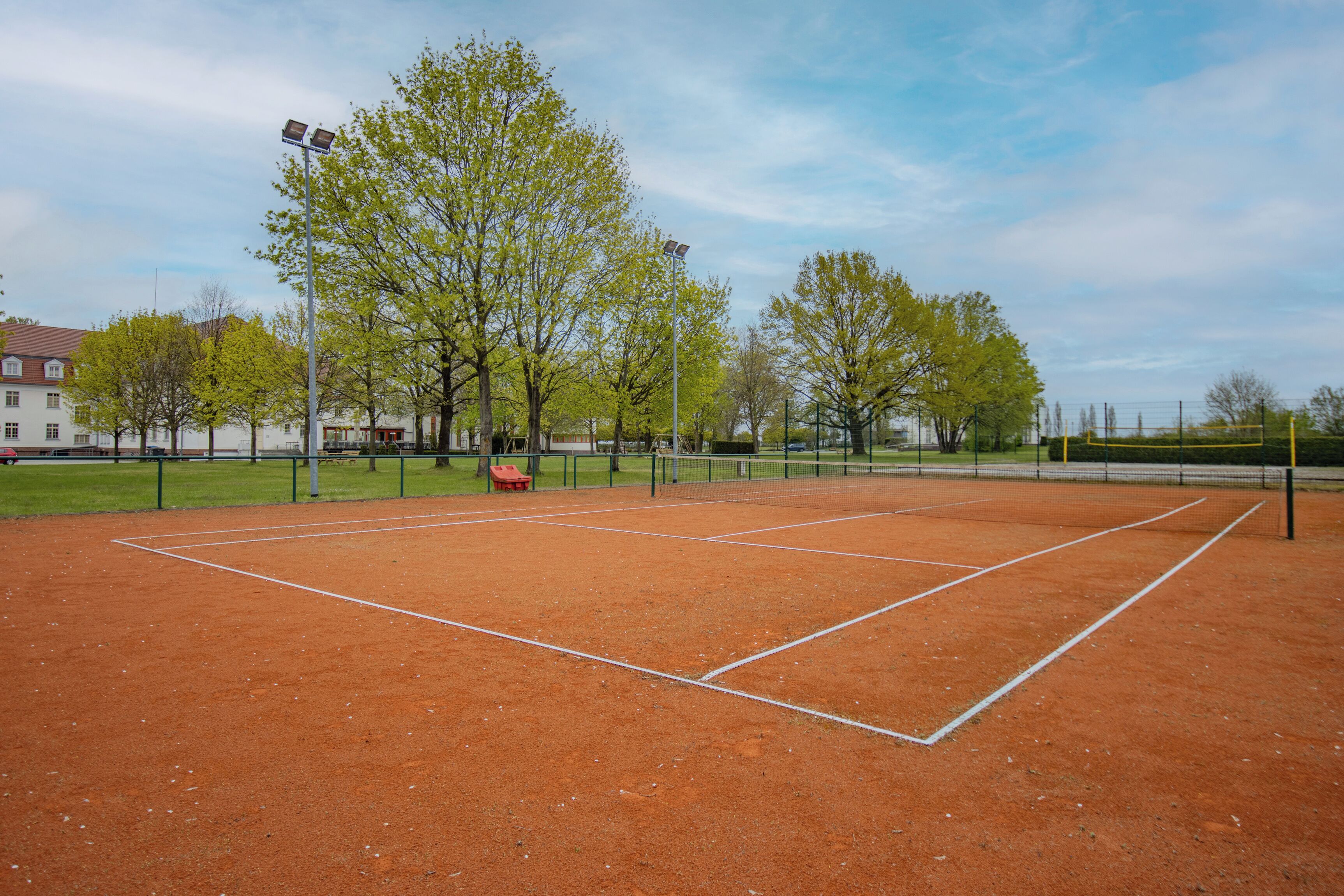 Una cancha de tenis con red, árboles y una valla.