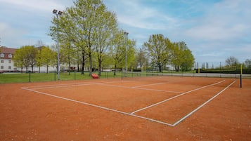 Una cancha de tenis con red, árboles y una valla.