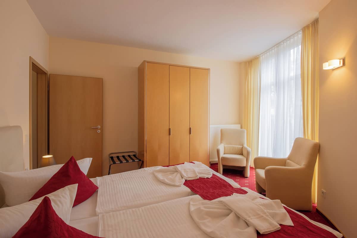 A hotel room with a bed, two chairs, a wardrobe, and a window with curtains.