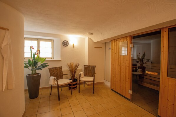 A room with a tiled floor, two wicker chairs, a potted plant, a clock on the wall, and a sliding door leading to another room.