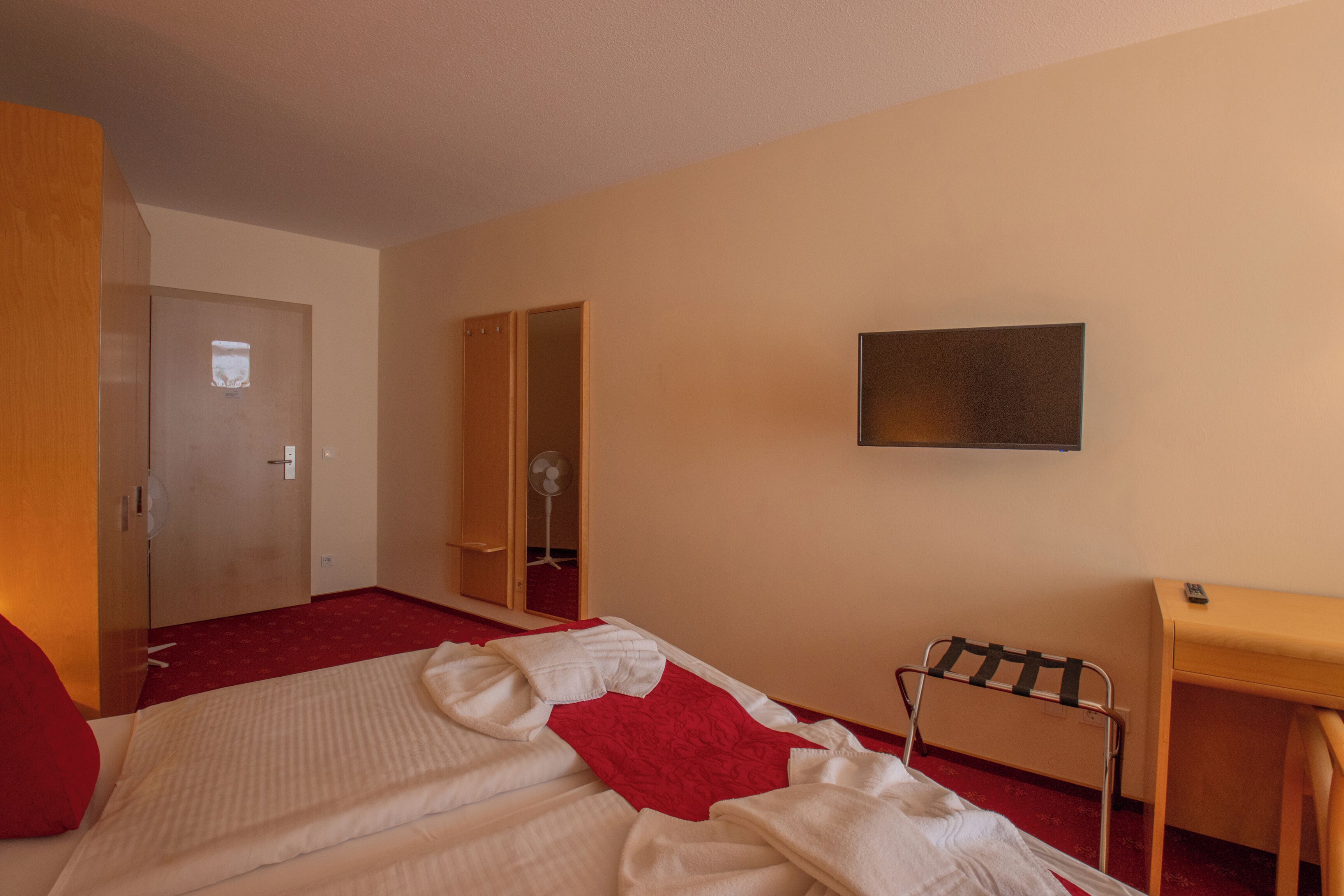 Ein Hotelzimmer mit Bett, Schreibtisch, Fernseher, Kleiderschrank und einer Tür.