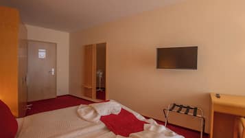Ein Hotelzimmer mit Bett, Schreibtisch, Fernseher, Kleiderschrank und einer Tür.