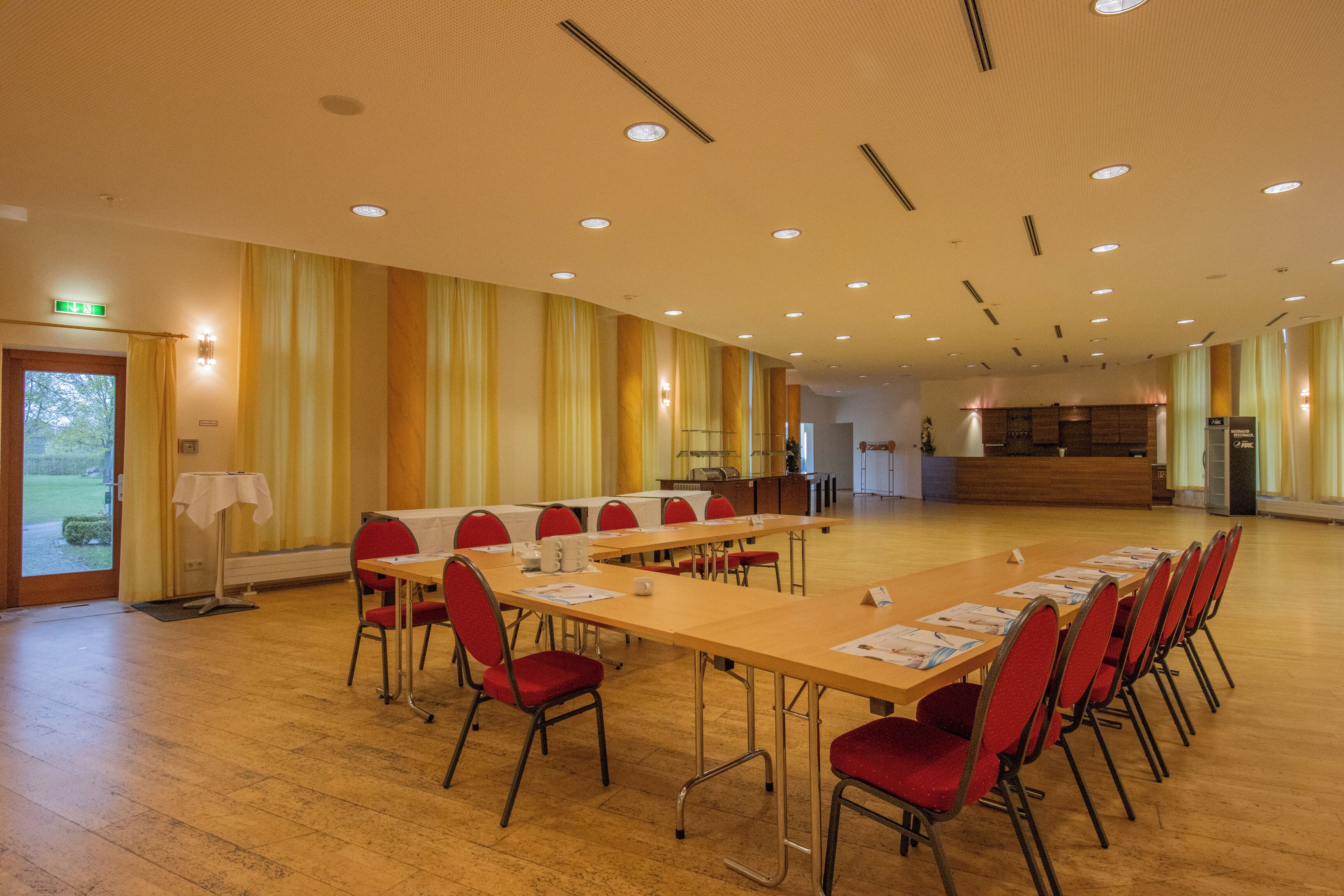 Ein Konferenzraum mit einem langen Tisch, roten Stühlen und einer Küchenzeile im Hintergrund.