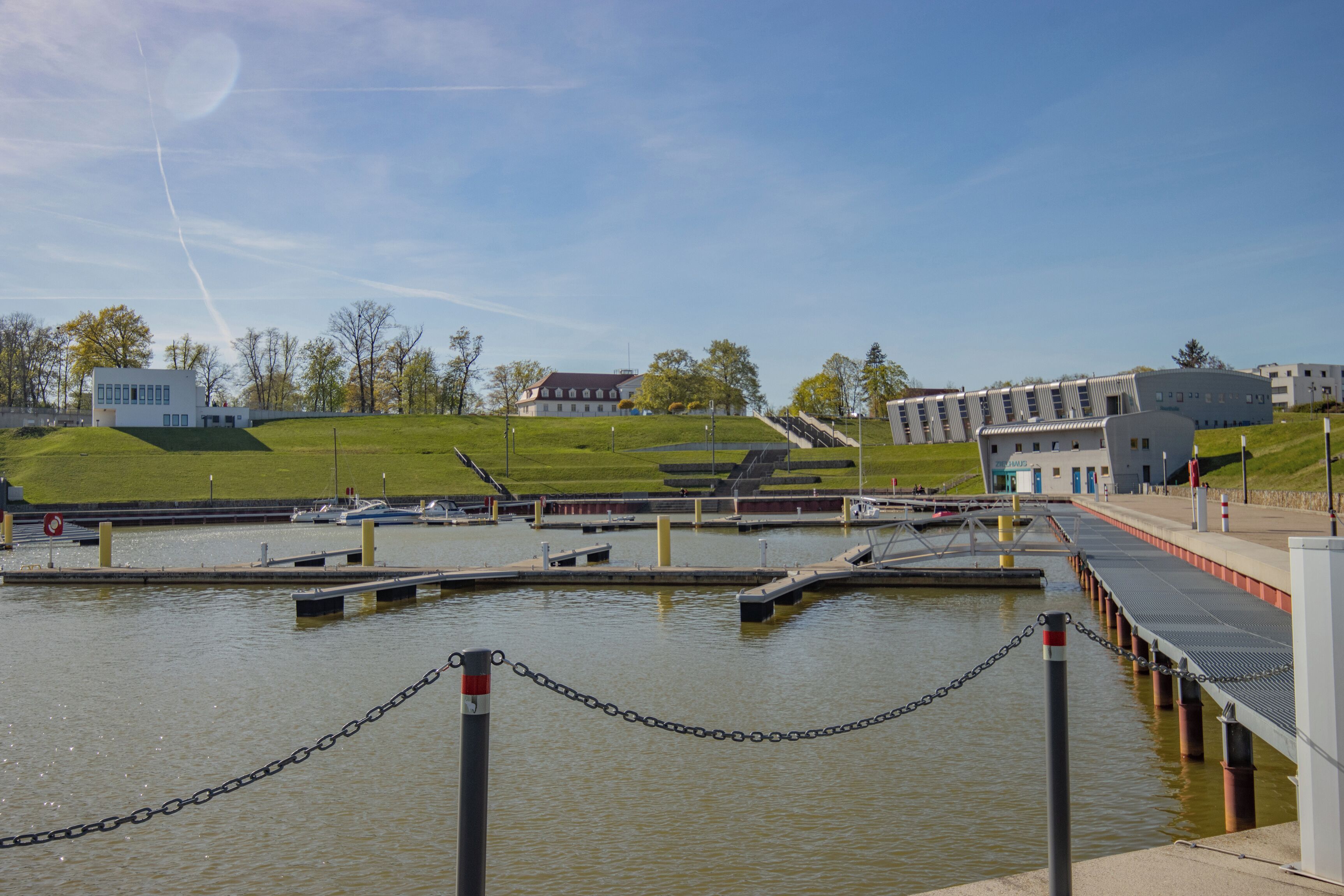 A waterfront property with a dock, a chain barrier, and a grassy area with buildings in the background.