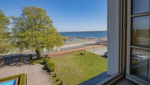A view from a window overlooking a grassy area with a tree, a pool, and a body of water. - Seehotel Grossraeschen (Großräschen)
