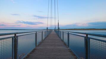 Un puente peatonal de madera con barandillas de metal que lleva a una masa de agua.