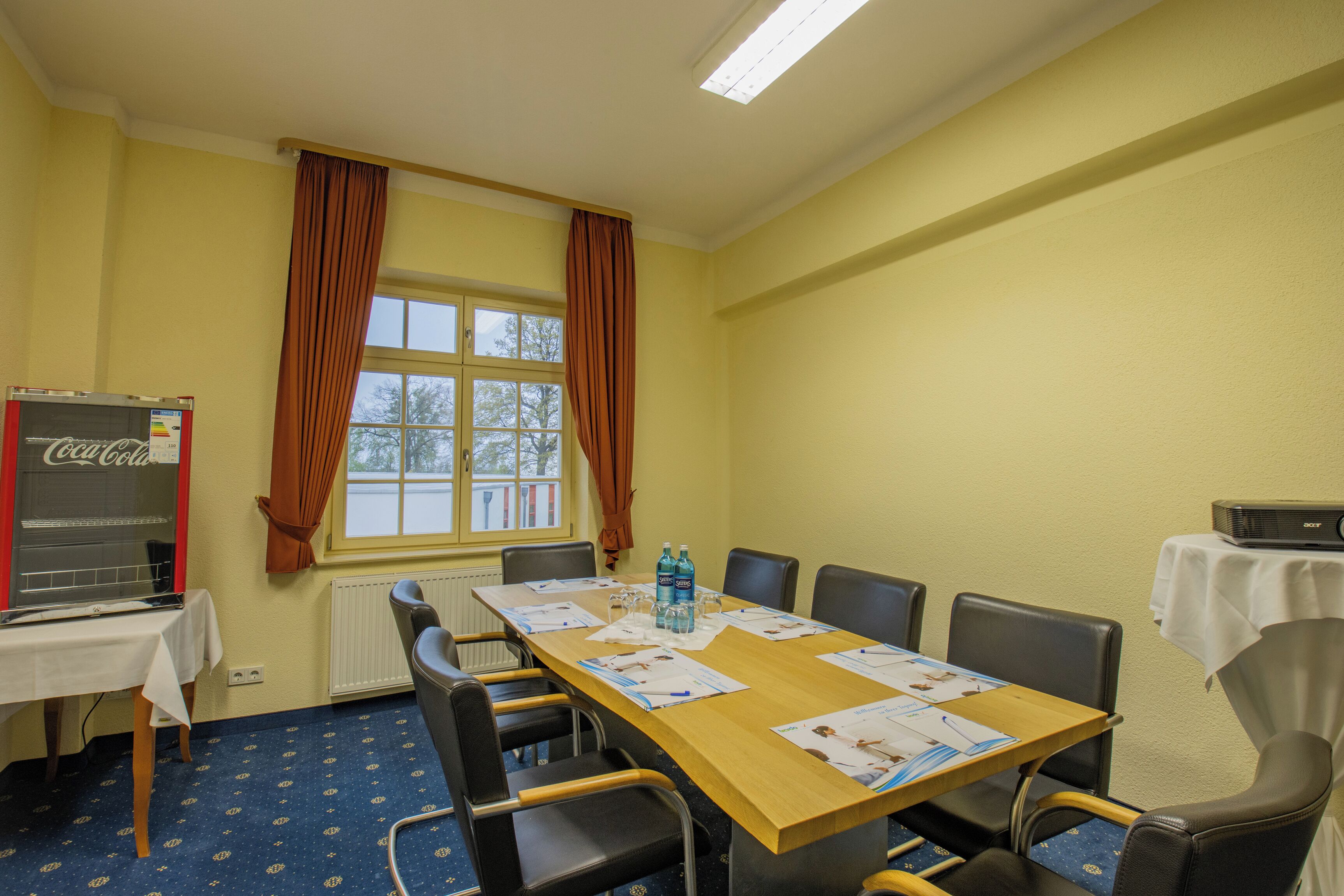 A conference room with a long table, chairs, a projector, and a Coca-Cola refrigerator.