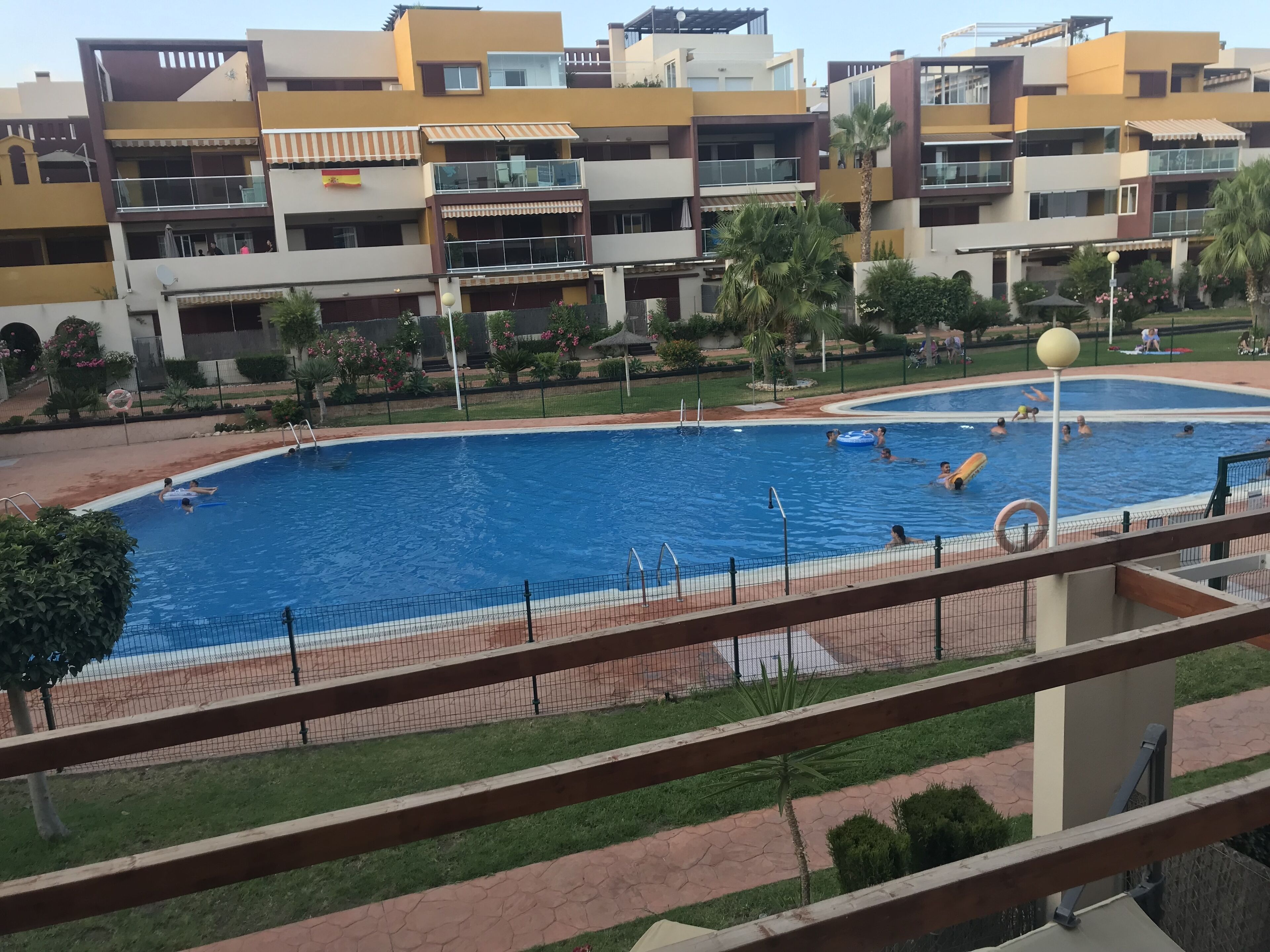 A swimming pool surrounded by a fence, with a view of multi-story buildings in the background.