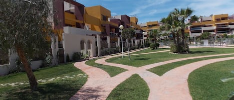 A courtyard with a paved walkway, greenery, and modern buildings with balconies.