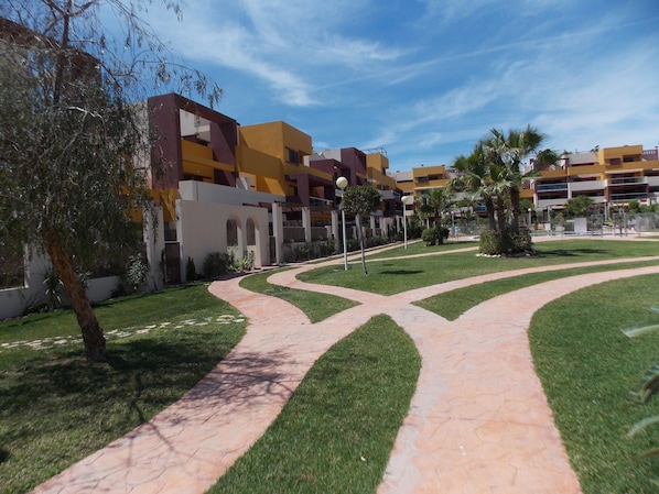 A courtyard with a paved walkway, greenery, and modern buildings with balconies.