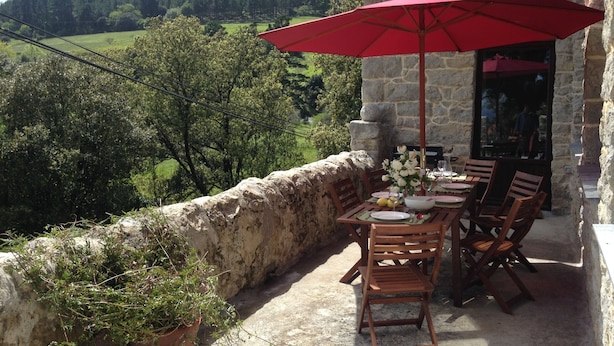An outdoor dining area with a stone wall, wooden chairs, a table, and a red umbrella. - Mountain and Sea, The Basque Country (Gardata Artika (Bizkaia))