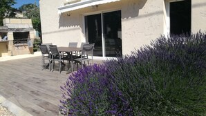 Ein Haus mit Terrasse, Grill und Tisch mit Stühlen.