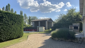 Ein Kiesweg führt zu einem Gebäude mit einer Steinaußenwand, einem Pool mit roten Stühlen und einem Grillplatz aus Stein.