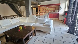 Ein Wohnzimmer mit einem weißen Modulsofa, einem Holztisch und einer Küche im Hintergrund.