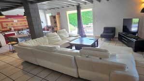 Ein großzügiger Wohnbereich mit einem weißen Ledersofa, einem Couchtisch, einem Fernseher und einem Klavier.