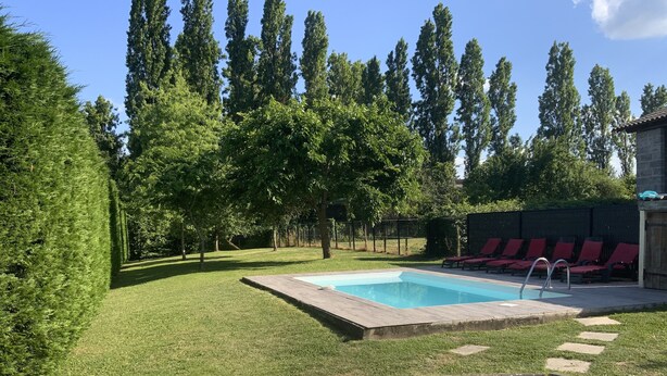 Ein rechteckiger Pool mit einer Holzterrasse, umgeben von einem gepflegten Rasen und roten Liegestühlen.