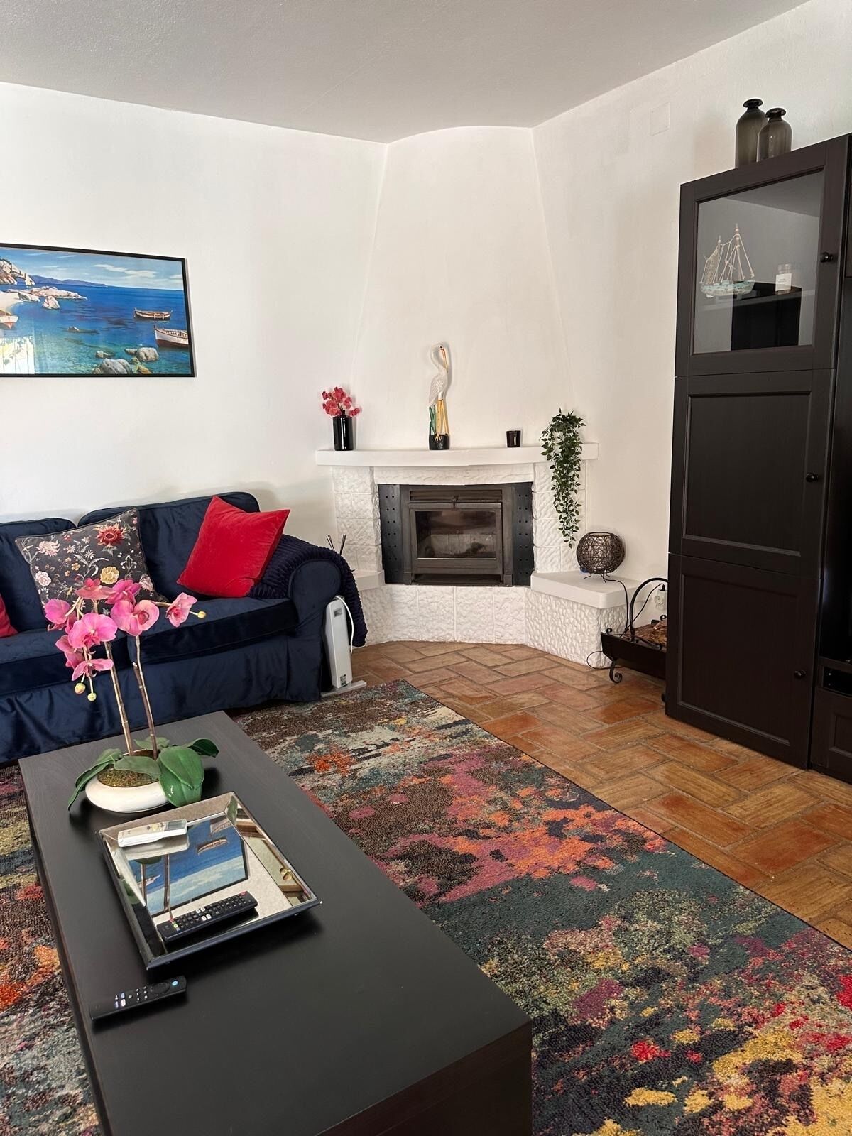 Ein Wohnzimmer mit Kamin, einer Couch, einem Couchtisch mit Fernbedienung und einem bunten Teppich.