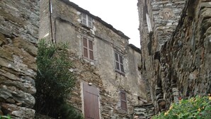 Un escalier étroit en pierre mène à un bâtiment rustique en pierre, doté d’une porte en bois et de fenêtres à volets.