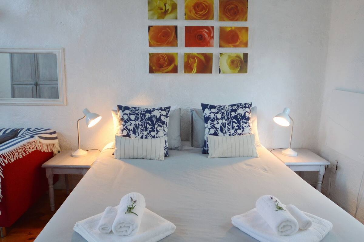 Ein Hotelzimmer mit einem großen Bett, zwei Nachttischen, einem roten Sessel und einer Wand mit floralen Bildern.