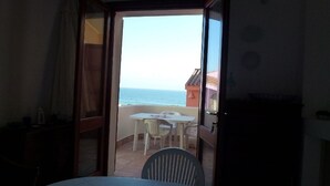 An open doorway leading to a balcony with a table and chairs, overlooking a beach and ocean.