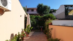 A narrow outdoor corridor with potted plants on both sides, leading to a building entrance.
