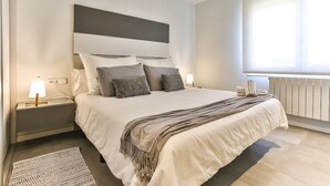 Ein modernes Schlafzimmer mit einem großen Bett, einem Nachttisch mit Lampe, einer Heizung und einem Fenster mit Jalousien.