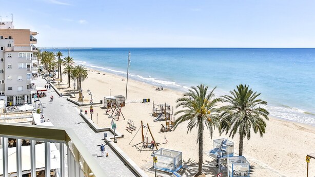 Ein Hotel direkt am Strand mit einer langen Promenade, Palmen und Meerblick.