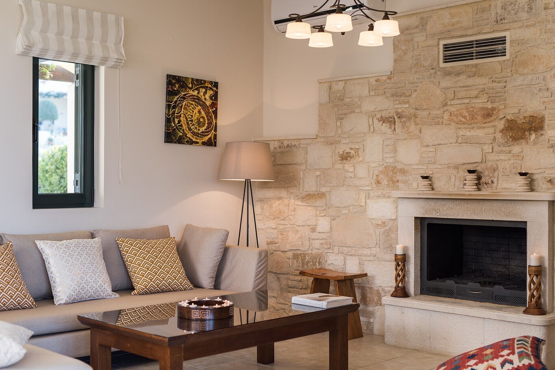Un salon doté d’une cheminée en pierre, d’un canapé agrémenté de coussins à motifs, d’un lampadaire et d’un lustre moderne.