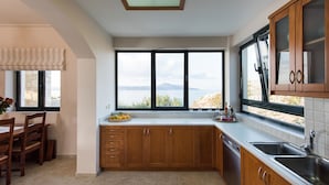 Uma cozinha moderna com armários de madeira, uma janela ampla com vista para o mar e um espaço de refeições com mesa e cadeiras.