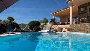 En klarblå pool med solstolar och en stenmur.