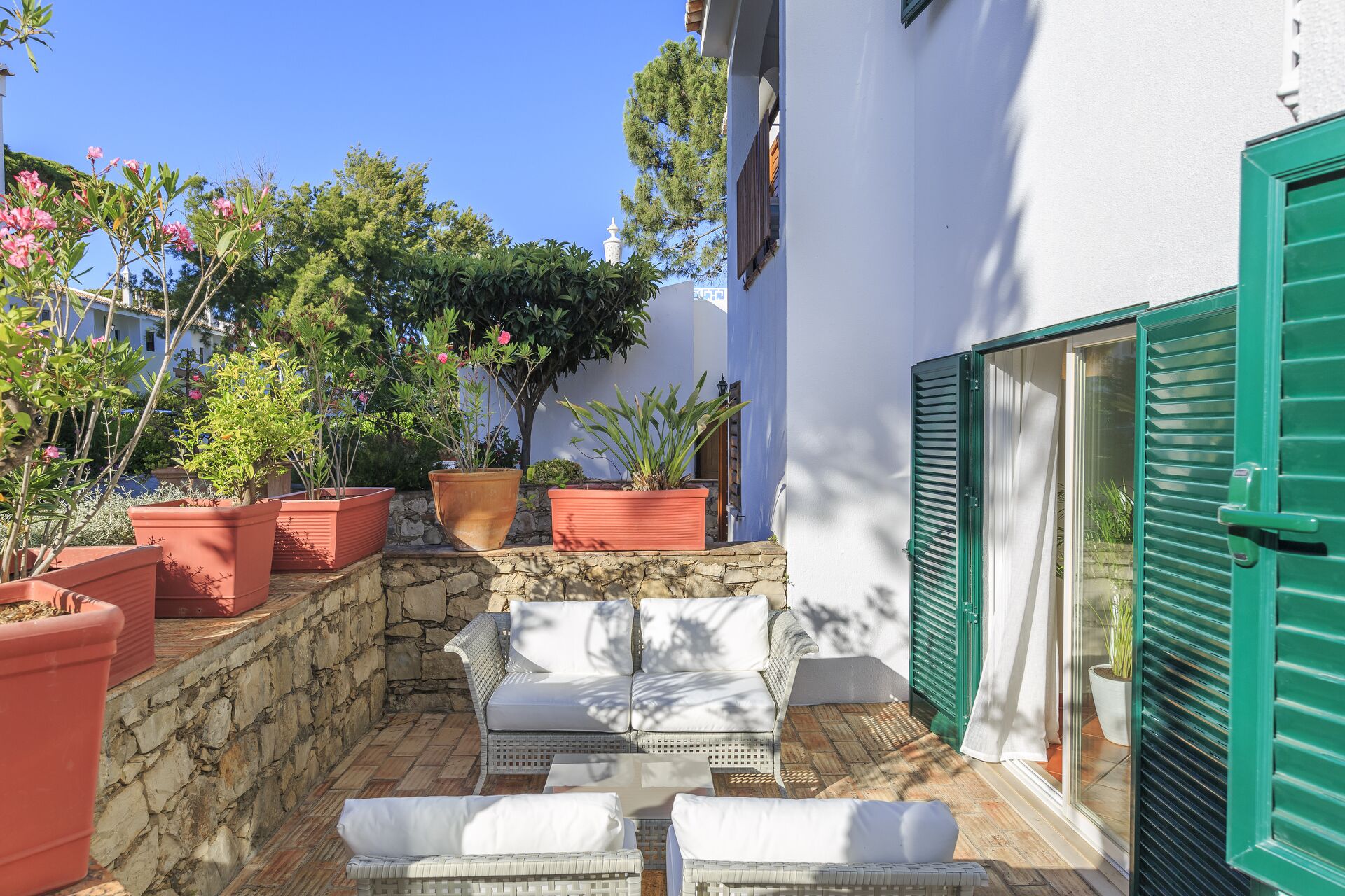 A small outdoor seating area with a stone wall, potted plants, and a white wicker sofa.