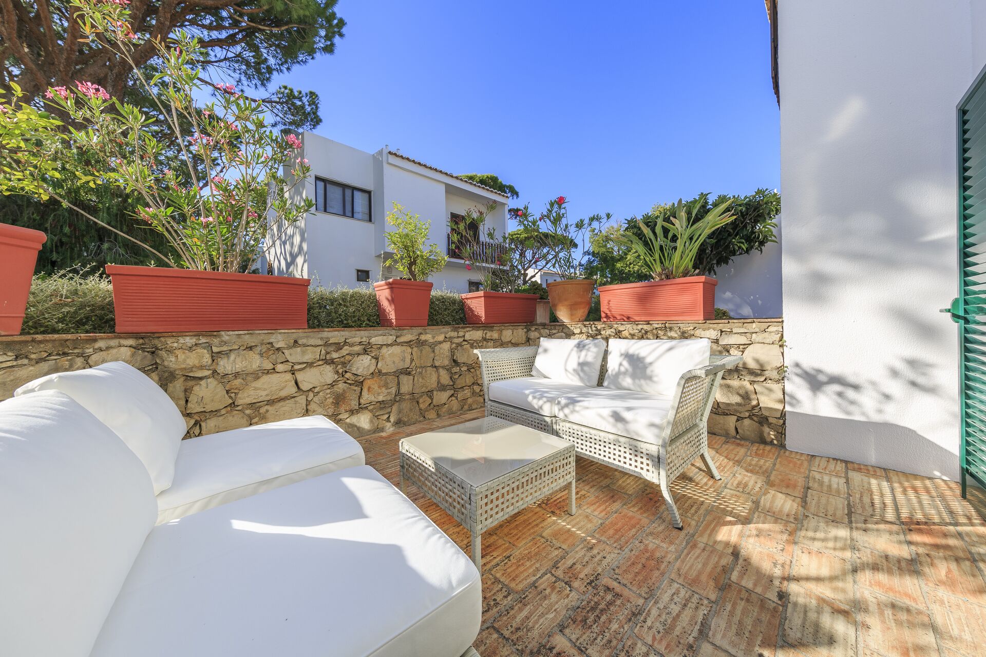 Un patio con mobiliario exterior blanco, un muro de piedra y plantas en macetas.