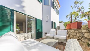 Eine Terrasse mit weißem Gartenmöbel, einer Steinmauer und einem Gebäude mit grünen Fensterläden.