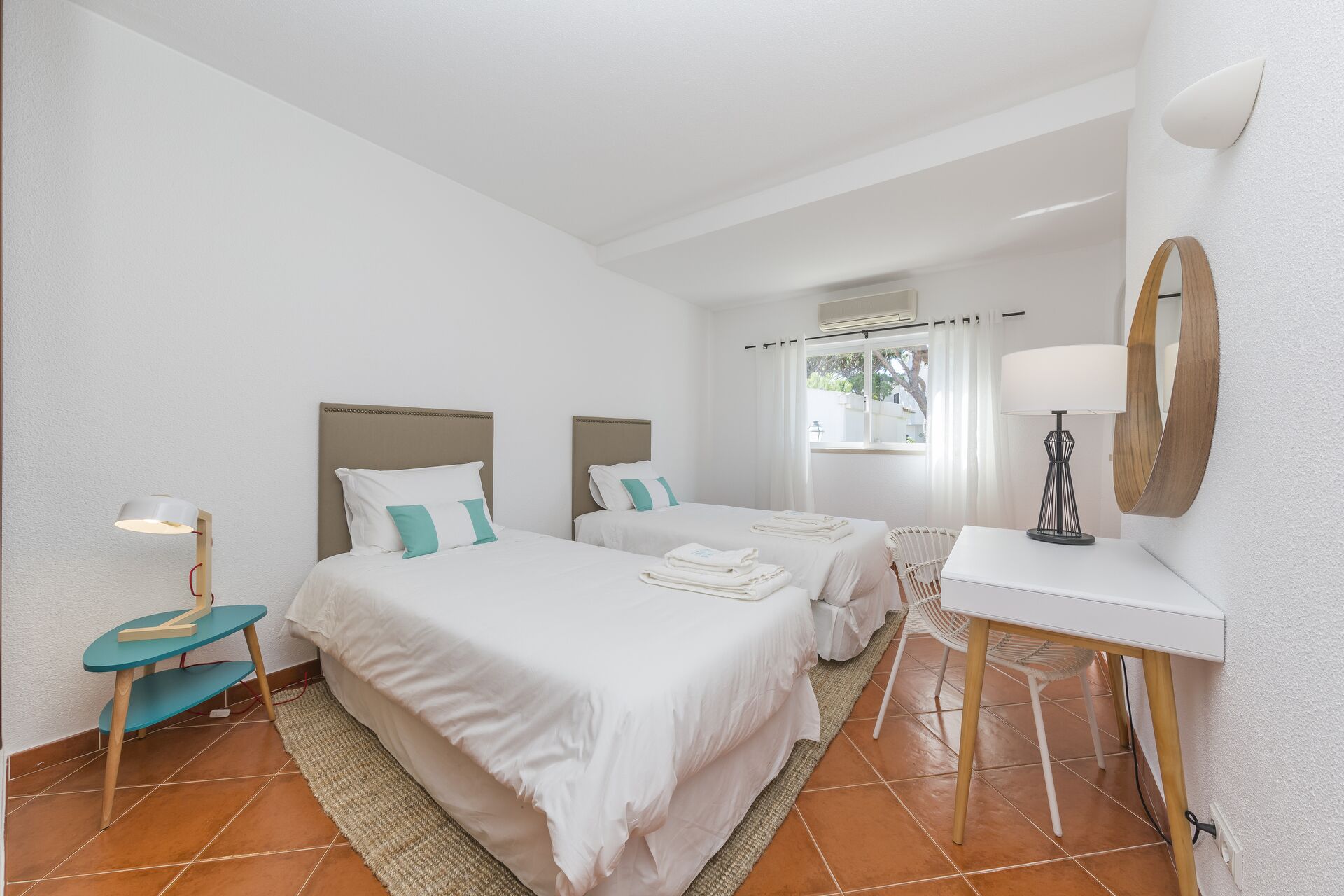 A hotel room with two beds, a desk, a chair, a lamp, and a mirror.