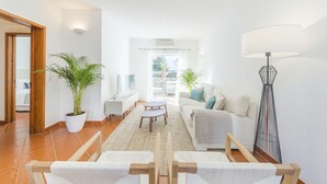 Ein geräumiger Wohnbereich mit einer Couch, einem Couchtisch und einem Fernseher. Eine Topfpflanze und eine Stehlampe sind ebenfalls vorhanden.