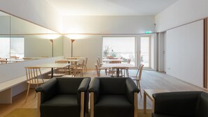 Een ruime kamer met een groot raam, een spiegel en meerdere tafels en stoelen.