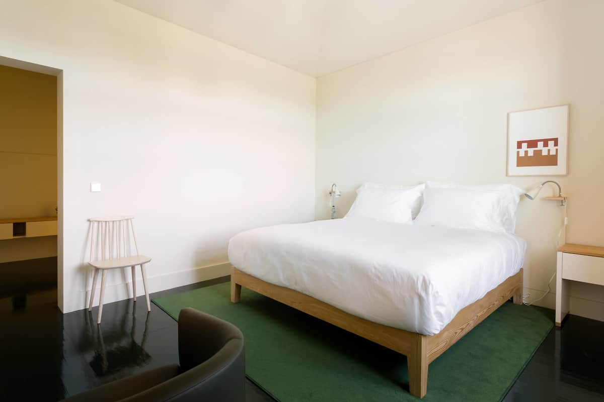 A minimalist bedroom with a single bed, a small chair, and a green rug.