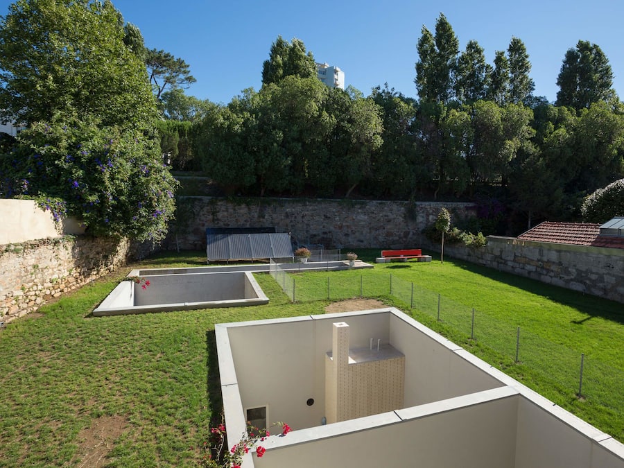 A landscaped area with a rectangular pool, a stone wall, and a grassy lawn.