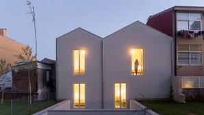 Een modern gebouw met twee verdiepingen, drie verlichte ramen, een omheinde tuin en een waslijn aan de rechterkant.